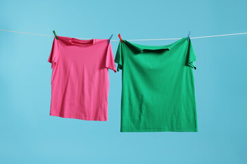 Two colorful t-shirts drying on washing line against light blue background
