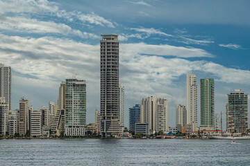 Fototapeta na wymiar Cartagena, Colombia - July 25, 2023: Tall luxury modern apartment buildings at Bocagrande Neighborhood under blue cloudscape. Tall ship docked at Naval Base 