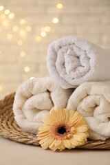 Rolled terry towels and flower on white table near brick wall indoors