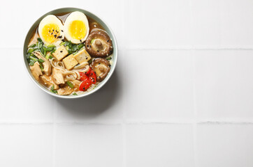 Noodle soup. Bowl of delicious ramen on white tiled table, top view. Space for text