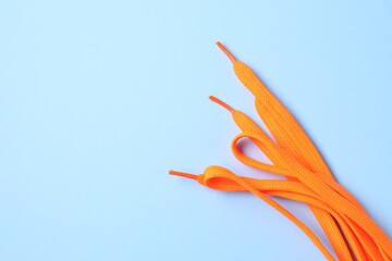 Stylish orange shoe laces on light blue background, top view. Space for text