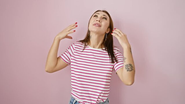 Frustrated young brunette girl in stripes tshirt, furious and mad, screaming crazily, arms flailing against isolated pink background