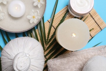 Flat lay composition with spa products, burning candle and beautiful flowers on light blue background