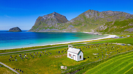 Beautiful norwegian wooden chapel with idyllic cemetery at the Haukland Beach with tropical clear water of the Atlantic Ocean. Haukland, Lofoten Islands, Norway. - obrazy, fototapety, plakaty