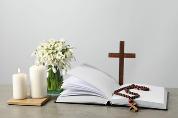 Church candles, Bible, wooden cross, rosary beads and flowers on grey table