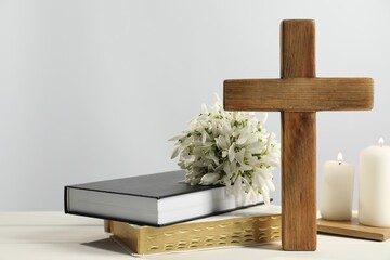 Burning church candles, wooden cross, ecclesiastical books and flowers on white table. Space for...