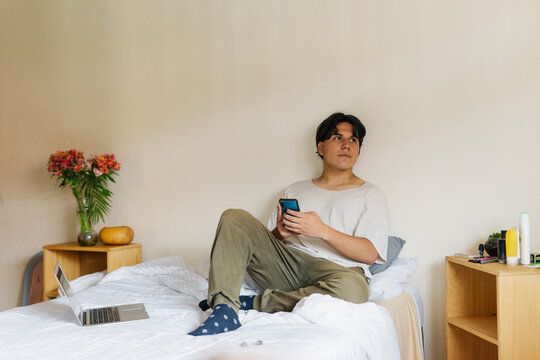 Young man sitting on the bed in his room.