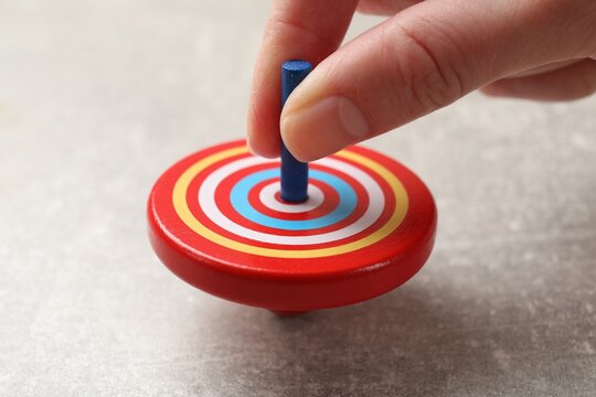 Woman playing with bright spinning top at grey textured background, closeup