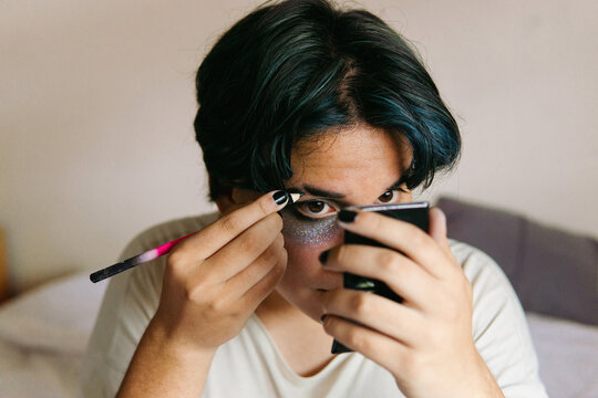 Teenage man applying makeup with eyeliner.