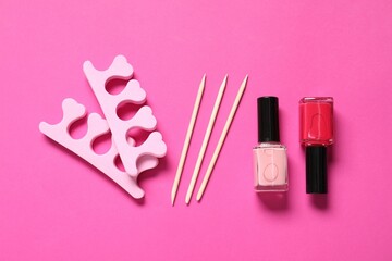 Nail polishes, orange sticks and toe separators on pink background, flat lay
