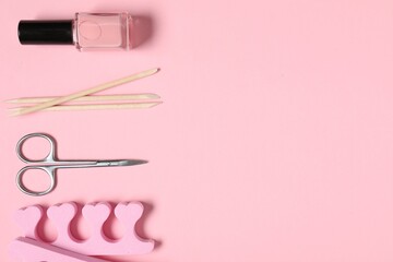 Nail polish, orange sticks, scissors and toe separators on pink background, flat lay. Space for text