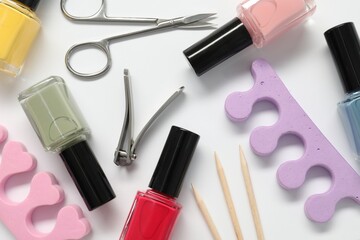 Nail polishes and set of pedicure tools on white background, flat lay