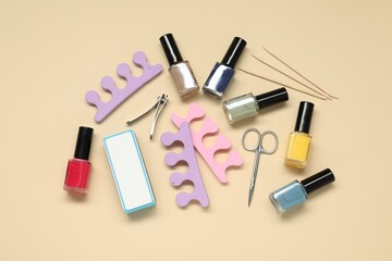 Nail polishes and set of pedicure tools on beige background, flat lay