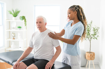 Fototapeta premium Black physiotherapist helping senior man with in clinic. Elderly man undergoing physiotherapy treatment for injury