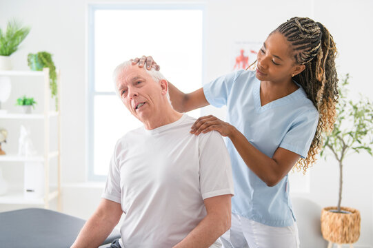 Black physiotherapist helping senior man with in clinic. Elderly man undergoing physiotherapy treatment for injury