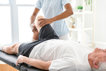 Obraz premium Black physiotherapist helping senior man with in clinic. Elderly man undergoing physiotherapy treatment for injury