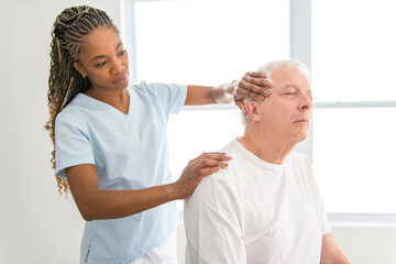 Fototapeta premium Black physiotherapist helping senior man with in clinic. Elderly man undergoing physiotherapy treatment for injury