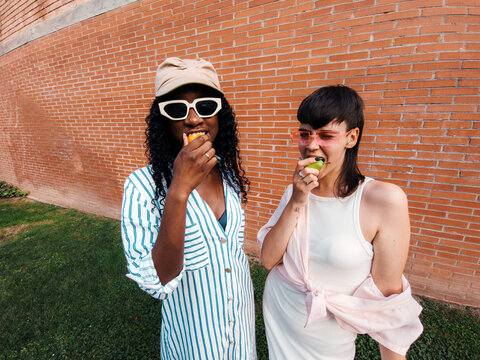 Two hungry young women biting fruit
