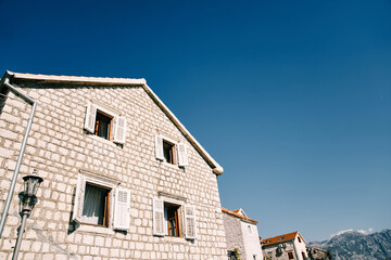 Fototapeta na wymiar Ancient stone house with white wooden open shutters against a blue sky
