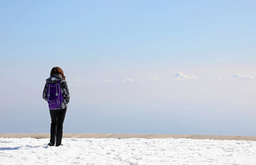 young girl hiker on the top of the mountain admires the panorama from the top of the peak on the white snow in winter - obrazy, fototapety, plakaty