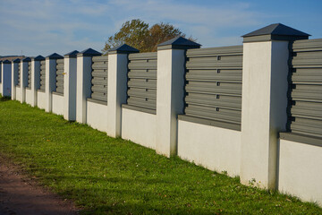 Obraz premium a fence made of a wall and a metal profile, a new fence made of metal profile with white columns has been built, protection of the territory