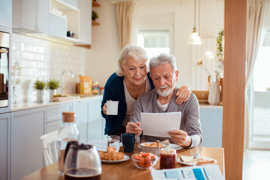 Senior couple reading bills at the kitchen table at home