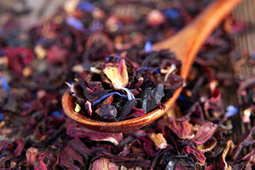 Tea mix of karkade, flowers and berries in a spoon and on the table.