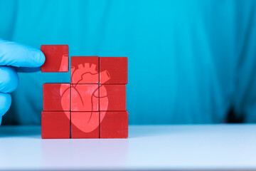 Concept of heart transplant and heart diseases, cardiomyopathy, arrhythmia. The doctor's hand organizes the wooden cubes. Heart donor.