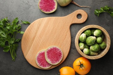 Flat lay composition with wooden cutting board and products on dark textured table