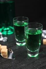 Absinthe in shot glasses, spoon and brown sugar cubes on gray table, closeup. Alcoholic drink