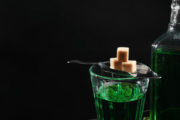 Absinthe in glass, brown sugar and spoon against black background, space for text. Alcoholic drink