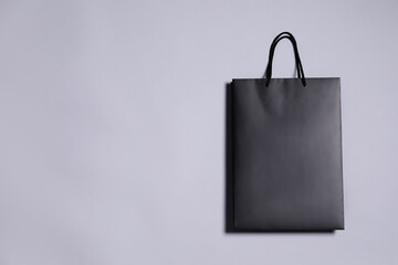 One black paper shopping bag on grey background, top view. Space for text