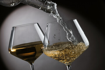 Pouring tasty aromatic wine in glass on gray background, closeup