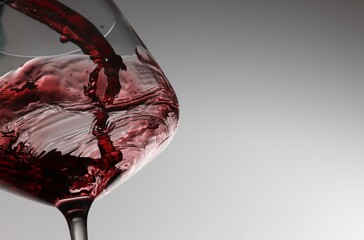 Pouring tasty red wine in glass on light background, closeup. Space for text