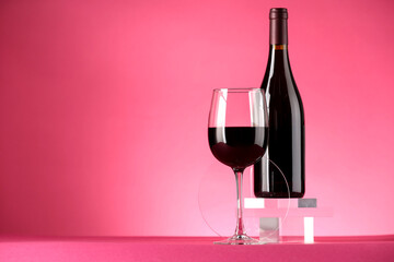 Stylish presentation of delicious red wine in bottle and glass on pink background. Space for text