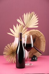 Stylish presentation of delicious red wine in bottle and glass on pink background