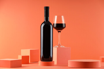 Stylish presentation of delicious red wine in bottle and glass on orange background