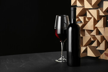 Stylish presentation of red wine in bottle and wineglass on table against black background, space...