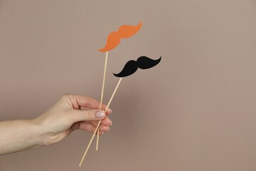 Woman with fake paper mustaches on beige background, closeup. Space for text