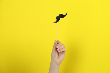 Woman with fake paper mustache on yellow background, closeup