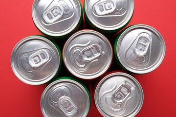 Energy drink in cans on red background, top view