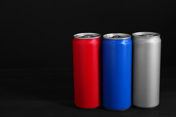 Energy drinks in colorful cans on black wooden table, space for text