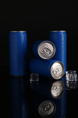 Energy drinks in wet cans and ice cubes on black background