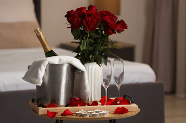 Honeymoon. Sparkling wine, glasses and bouquet of roses on wooden table in room