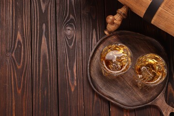 Fototapeta premium Whiskey with ice cubes in glasses and barrel on wooden table, top view. Space for text