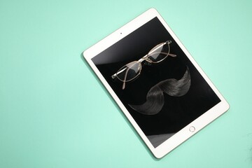 Artificial moustache, tablet and glasses on turquoise background, top view. Space for text