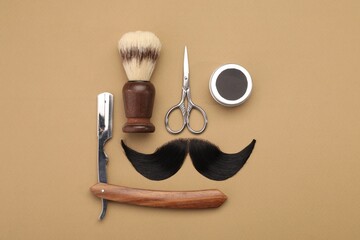 Artificial moustache and barber tools on beige background, flat lay