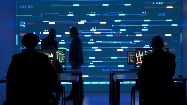 Technical support team in control room. Man and woman specialists discussing work, digital screen shows infrastructure monitoring infographic network data.