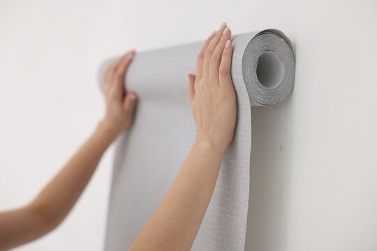 Woman hanging gray wallpaper in room, closeup