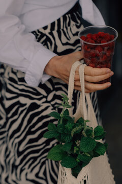 A container with raspberries and mint branches in a girl&rsquo;s hand